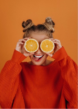 Sophie smiling with her tongue out, holding orange slices over her eyes