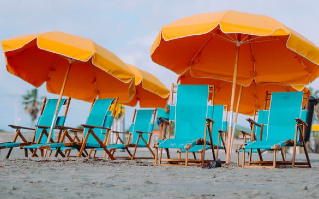 A beach with teal chairs and yellow umbrellas